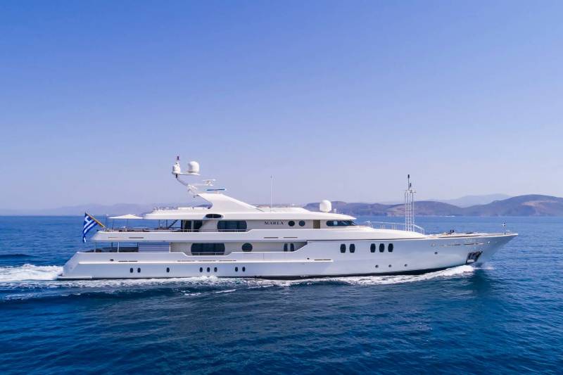 A large white yacht named MARLA cruises through the deep blue Aegean Sea under a clear sky.
