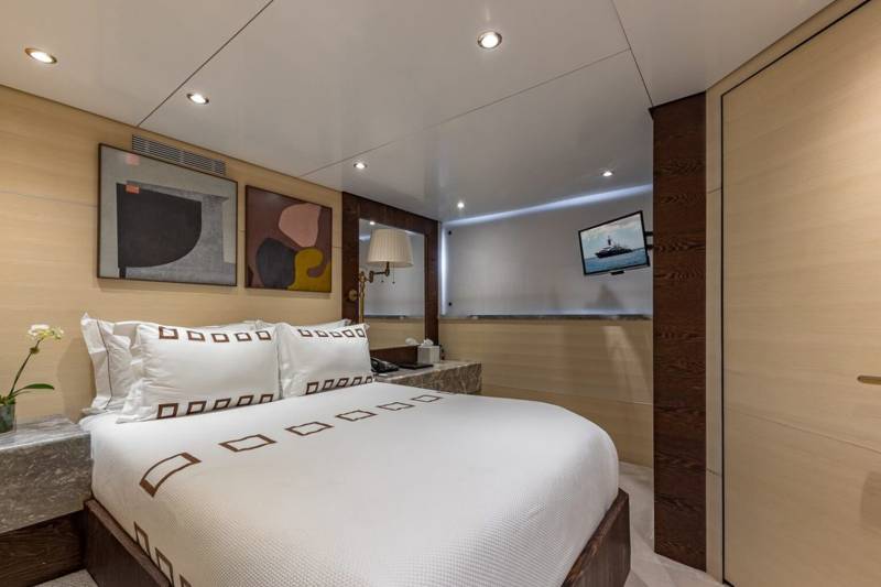 A luxurious yacht stateroom features a comfortable bed, modern art, and a wall-mounted television.