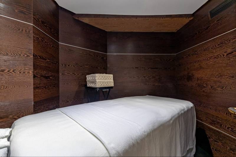 A massage table draped in white linens awaits in a room with rich, dark wood paneling.