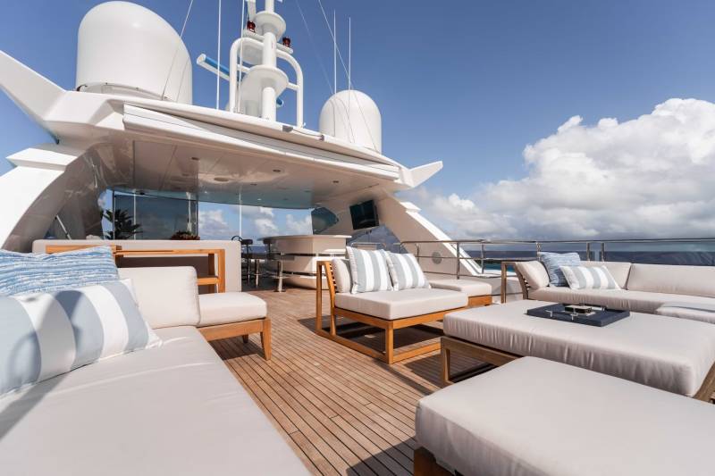 A luxurious yacht deck with comfortable seating arrangements, surrounded by a clear blue sky and fluffy white clouds.
