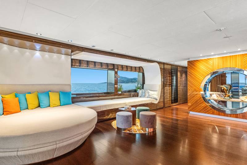 Luxurious yacht interiors feature a curved sofa with vibrant pillows and a circular display showcasing nautical treasures against a backdrop of the sea.