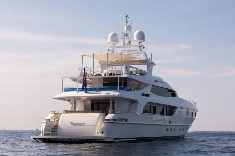 A luxurious white yacht glides across the calm blue sea under a bright, cloudy sky.