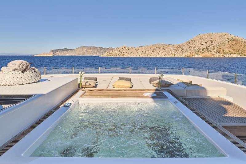 A luxurious yacht with a glass-enclosed pool on the deck, surrounded by stunning mountainous landscapes and the serene blue waters of the ocean.