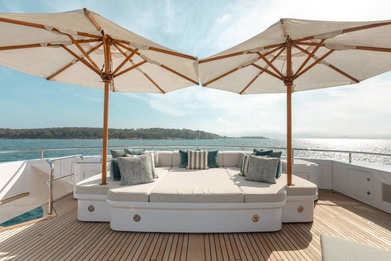 Luxurious outdoor seating on a yacht deck is shaded by two large umbrellas, offering a serene spot to enjoy the sparkling ocean view.