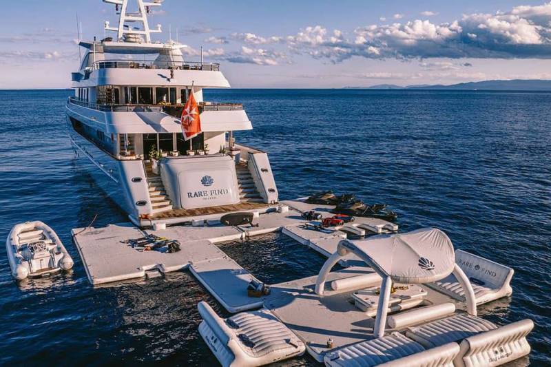 A luxurious superyacht anchors offshore, its inflatable deck and water toys creating a floating paradise.