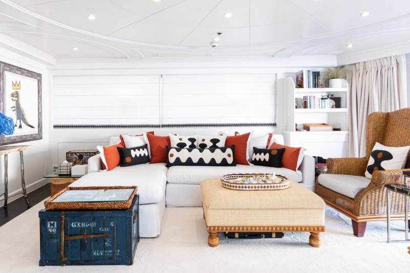 A modern living room features a white sectional sofa adorned with colorful pillows, a woven armchair, and a striking piece of abstract art.