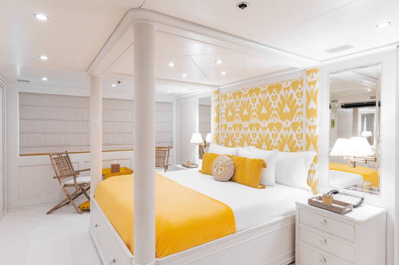 A luxurious yacht cabin features a vibrant yellow and white ikat-patterned headboard and a plush yellow throw on a grand four-poster bed.