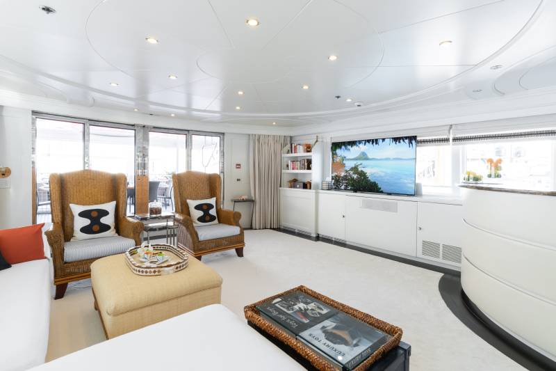 Relax in this luxurious yacht salon, featuring comfortable wicker chairs, a large television, and access to an outdoor deck.
