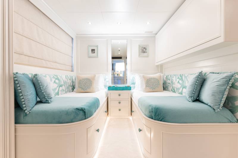 Luxurious twin beds with turquoise accents and coral-themed pillows create a serene retreat in this elegant cabin.
