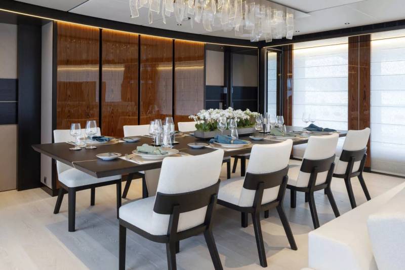 Elegant white chairs surround a dark wood dining table set with fine china and a floral centerpiece in this luxurious yacht interior.