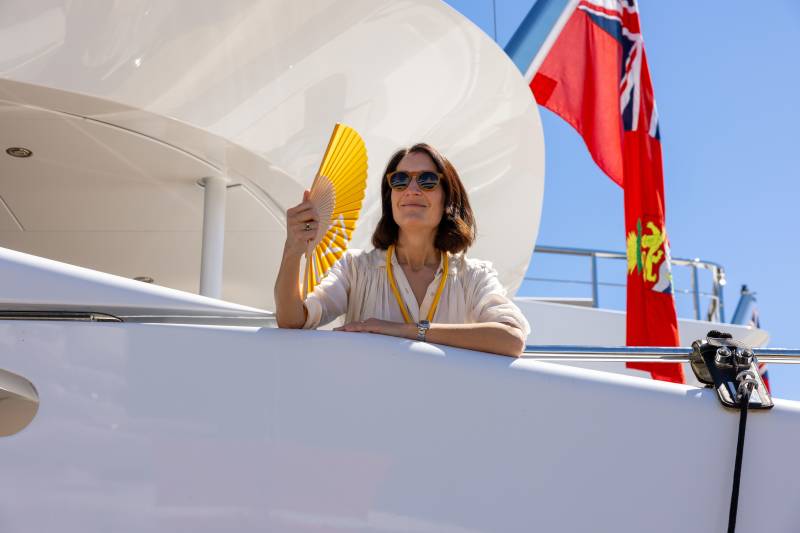 A woman enjoys a sunny day on a yacht, fanning herself with a bright yellow fan.