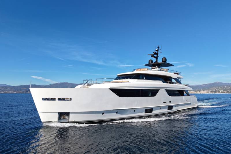 A sleek white yacht glides through the deep blue ocean under a clear sky dotted with wispy clouds.