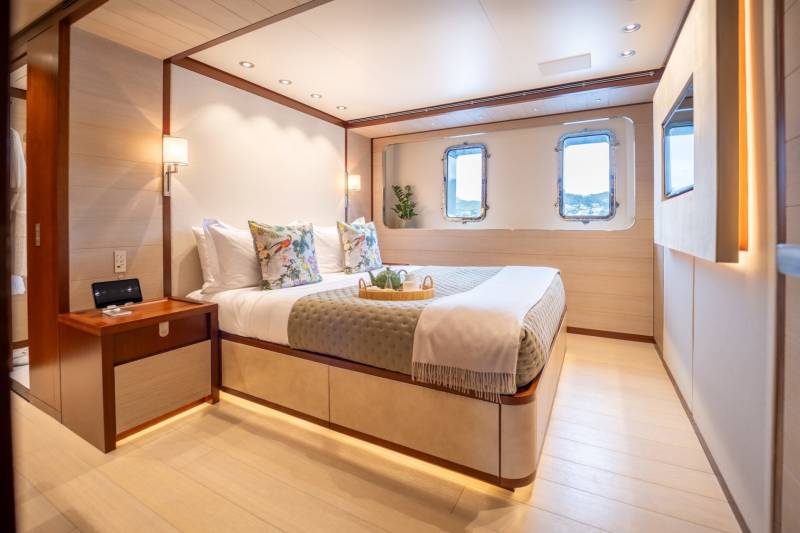 Luxurious yacht cabin features a comfortable bed, decorative pillows, and porthole windows offering scenic views.