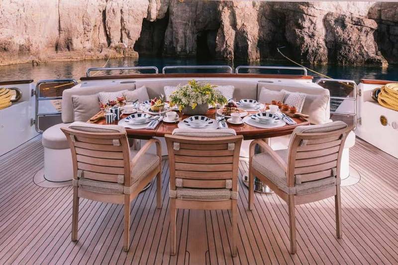 A beautifully set table awaits guests on the deck of a yacht, surrounded by stunning coastal scenery.