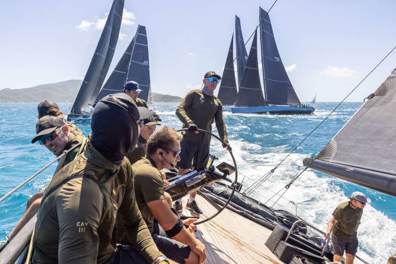 Sailors navigate choppy turquoise waters under a bright blue sky as they race their sleek yachts.