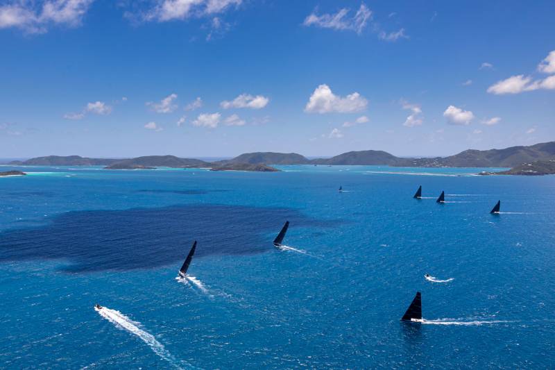 Black-sailed yachts race across the turquoise waters of the British Virgin Islands under a brilliant blue sky.