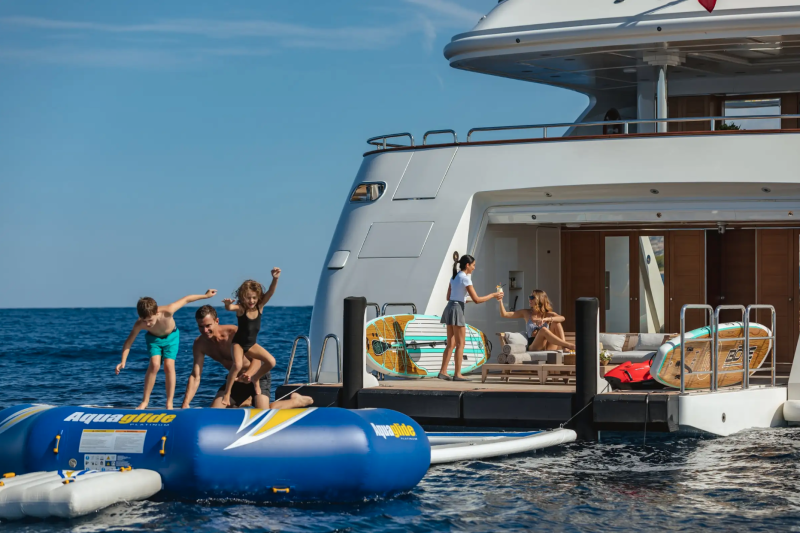 A family enjoys a sunny day of fun and relaxation on an inflatable water toy beside a luxurious yacht.