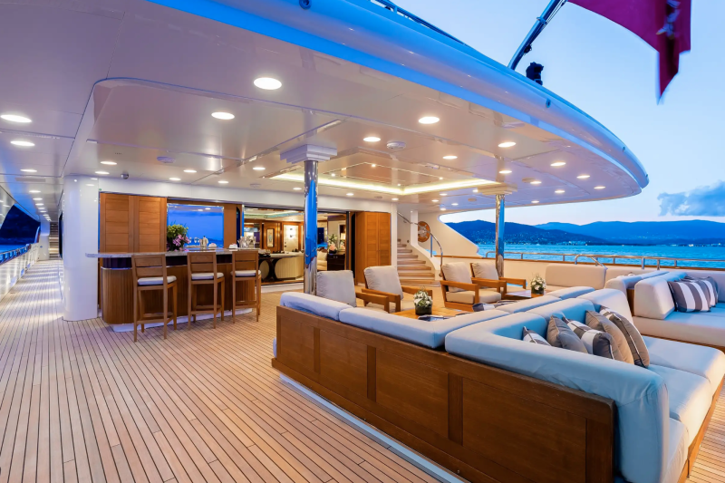 Luxurious outdoor seating and a bar area on a yacht deck offer a perfect setting for evening relaxation with a view of the coast.