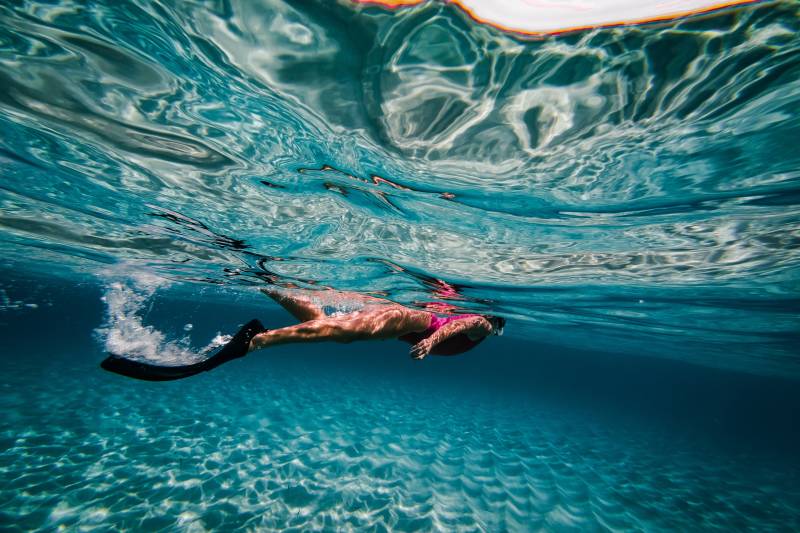 A snorkeler glides through crystal-clear turquoise waters, sunlight dappling the sandy seabed below.