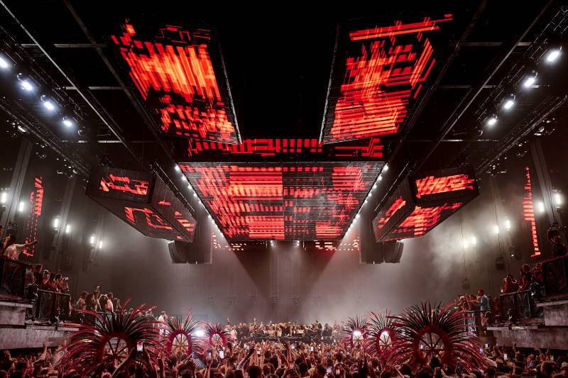 A massive crowd erupts in excitement under a dazzling display of red lights at a vibrant concert.