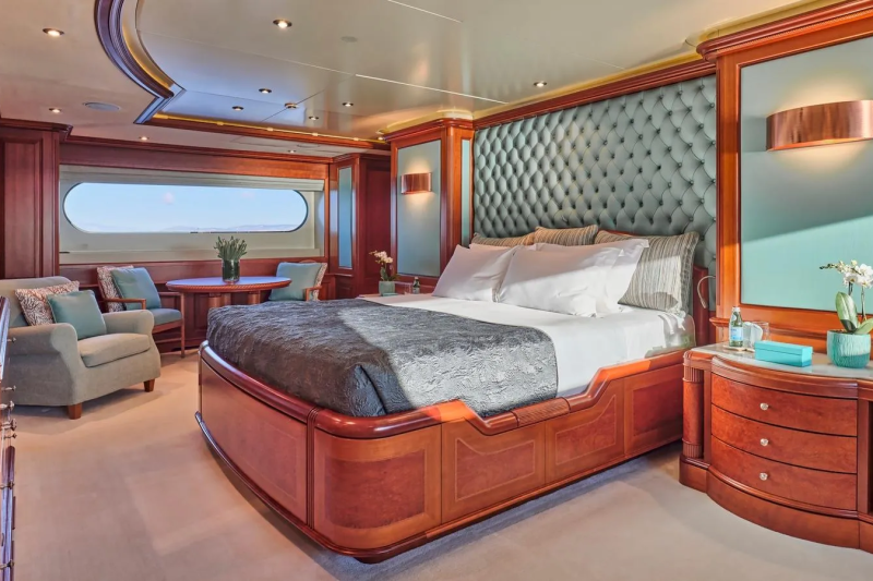 Luxurious yacht stateroom features a tufted headboard, plush bedding, and elegant wood finishes with a view of the sea.