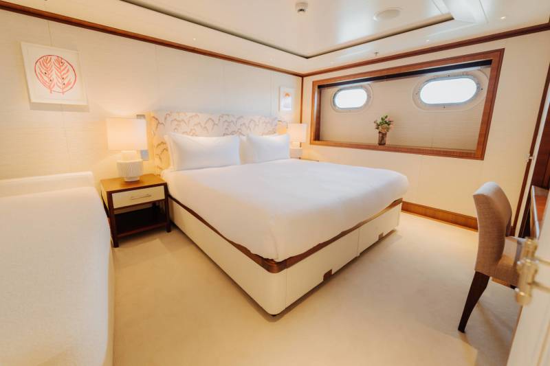 A luxurious yacht stateroom features a plush bed, elegant artwork, and porthole windows offering serene ocean views.