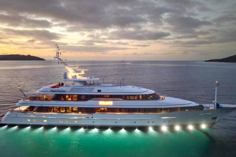 A luxurious yacht named Solace glows with warm interior lights and underwater illumination at dusk.