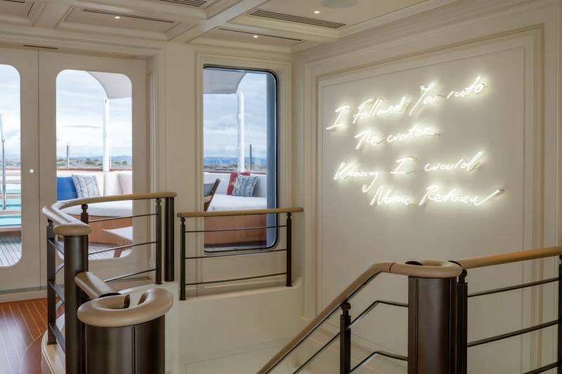 A modern and elegant interior space with large windows offering a scenic view, featuring a staircase with metal railings and a decorative lighting installation on the wall.