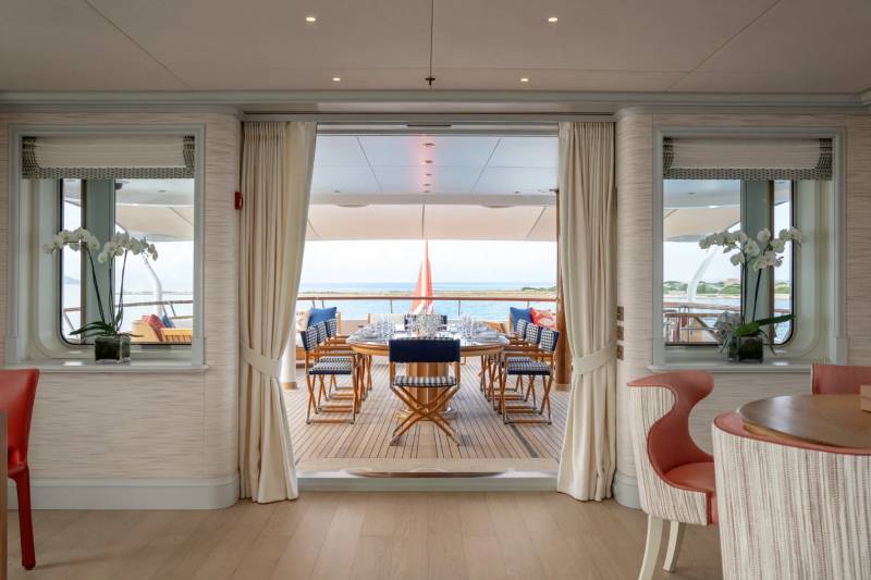 A cozy and inviting indoor dining area with large windows overlooking a wooden deck and the water beyond, creating a serene and picturesque setting.