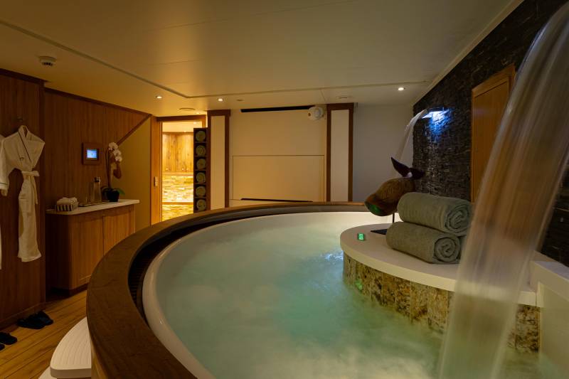 A luxurious spa-like bathroom with a large circular bathtub filled with water, surrounded by wooden and stone elements, creating a serene and relaxing atmosphere.
