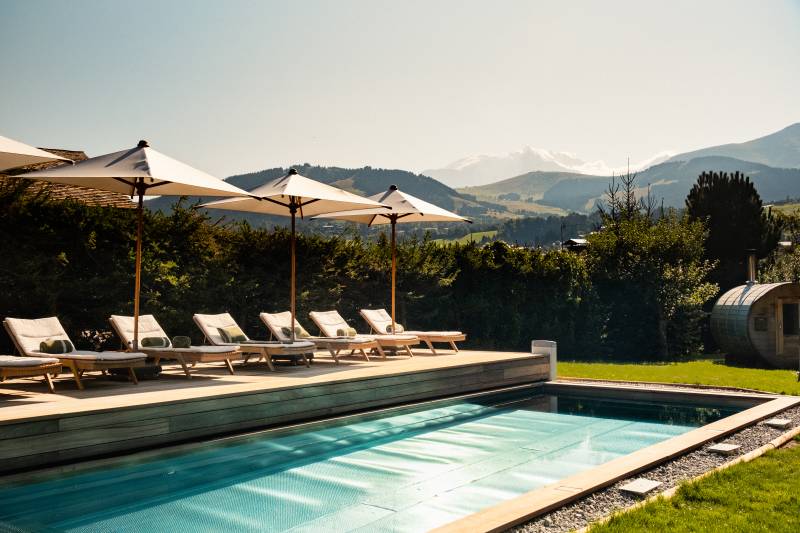 A hand pours rosé wine into a glass at a table set for a meal overlooking the sparkling blue sea.