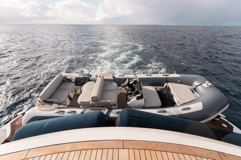 A large inflatable boat with several seats and a wake trailing behind it, surrounded by the vast expanse of the open ocean under a cloudy sky.