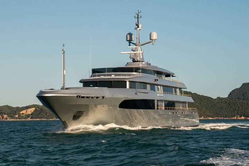 A large, luxurious yacht navigates the open waters, surrounded by a picturesque coastal landscape in the background.