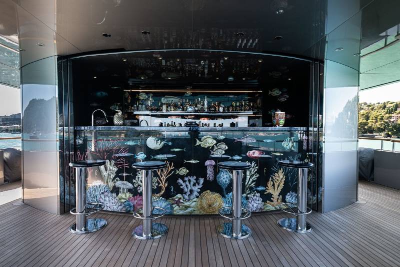 A modern and stylish bar with a glass-enclosed aquarium display in the foreground, showcasing various marine life, while the background features a panoramic view of a cityscape.