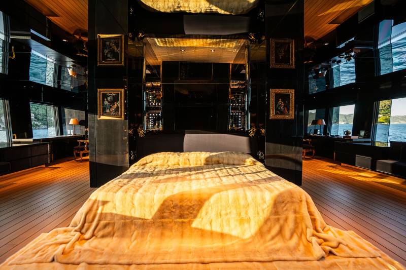 A cozy and inviting bedroom with a large bed covered in a warm, golden blanket, surrounded by dark wooden furniture and framed artwork on the walls, creating a luxurious and intimate atmosphere.