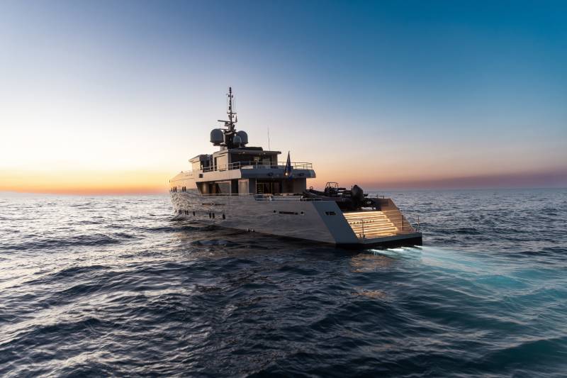 A large white yacht sailing on the calm, blue ocean at sunset, with a clear sky in the background.