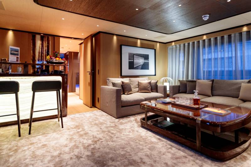 A luxurious lounge area with a bar in the foreground and a seating area with a large sofa and coffee table in the background.