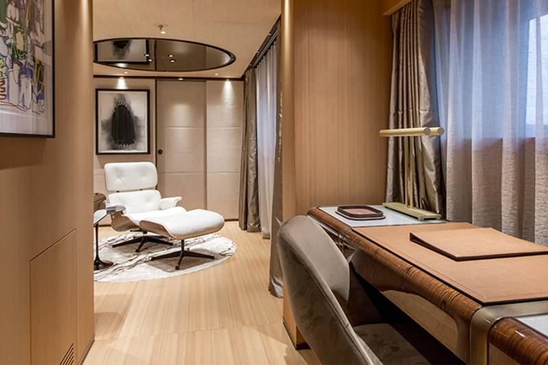 A modern office space features a desk with a chair in the foreground and a lounge chair with artwork in the background.