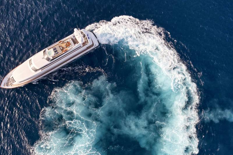 A luxurious white yacht cuts through the deep blue ocean, leaving a frothy white wake behind it.