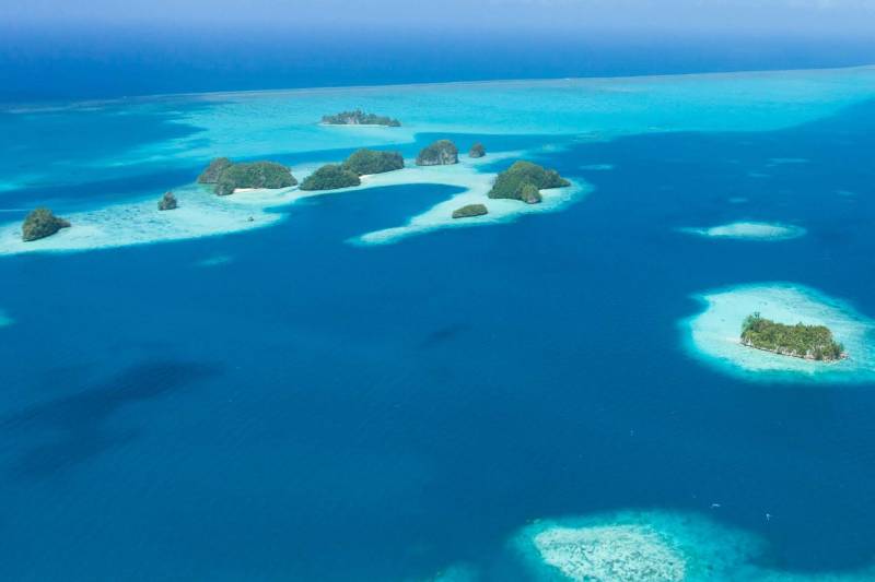 Lush green islands dot the vibrant turquoise waters of a tropical lagoon, with a clear blue sky stretching into the distance.