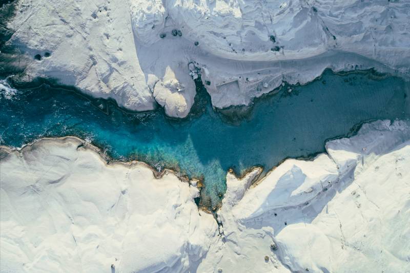 A vibrant blue river flows through stark white, rocky cliffs under a bright sky.