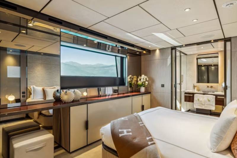 A luxurious bedroom with a large bed in the foreground and a scenic view through a wide window in the background.