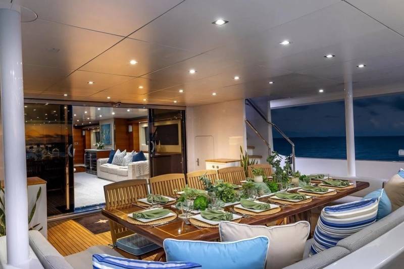 A beautifully set dining table on a yacht's deck is in the foreground, with the ocean and a twilight sky visible in the background.
