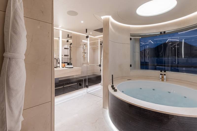 A plush white robe hangs on a tiled wall in the foreground, while a luxurious circular jacuzzi with a scenic view fills the background.