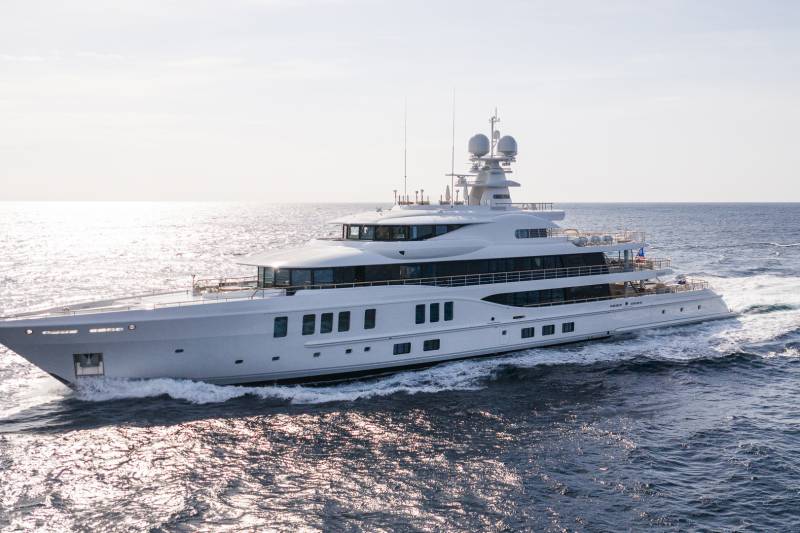 A large white yacht cruises through calm, sun-dappled ocean waters under a bright sky.