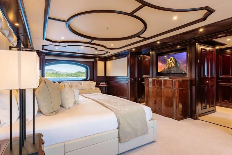 A luxurious bedroom with a large bed in the foreground and a television screen in the background, all set within a richly decorated interior.