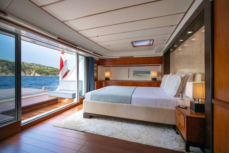 A luxurious bedroom with a large bed and a view of the ocean and a green coastline through a sliding glass door.