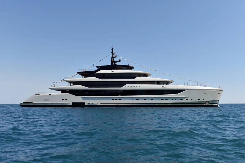 A large, white luxury yacht with multiple decks sails on calm blue water under a clear sky.
