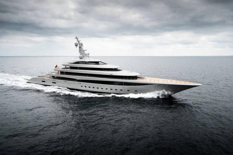 A large, modern yacht cruises through dark, choppy waters under a cloudy sky.