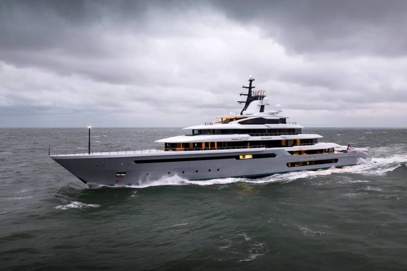 A large, modern gray yacht cruises through choppy, dark water under a cloudy sky.